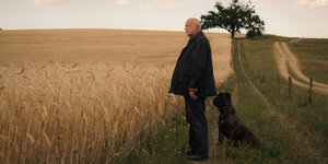Szene aus der Serie: Mann mit Hund steht auf einem Feld