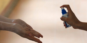 Eine Person sprüht Desinfektionsmittel auf Hände einer anderen Person