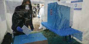 Eine Wählerin mit Mundschutz steckt ihren Wahlzettel in die Urne.