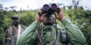 Ein Uniformierter schaut durch ein fernglas, im Hintergrund ein anderer mit Gewehr