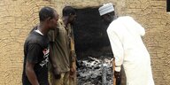 Männer betrachten ein ausgebranntes Haus in Nigeria.