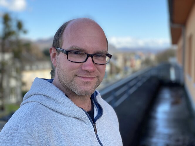 Ein Mann mit Brille vor Bahngleisen