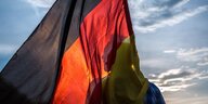 Ein Mann steht vor blauem Himmel und wird von einer großen Deutschlandfahne verdeckt