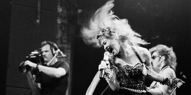 Schwarz-weiß-Bild, Cyndi Lauper mit Mikro und wehenden Haaren auf der Bühne