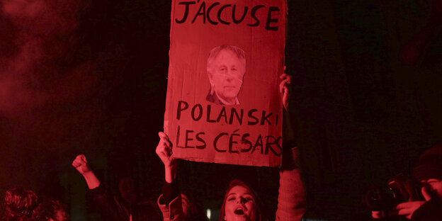 Ein junge Frau hält ein Pappschild hoch. Aufschrift: "J'accuse Polanski".