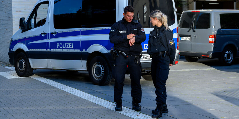 Polizist und Polizistin stehen vor Mannschaftswagen