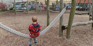 Ein Kind sitzt auf einem Seil auf einem Spielplatz