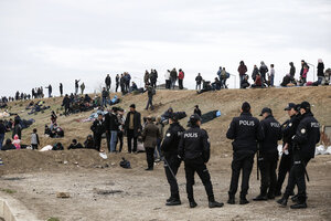 Flüchtlinge und Polizisten stehen auf einer Erderhöhung an der türkisch-griechischen Grenze.