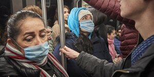 Menschen in einer überfüllten U-Bahn halten sich an Stangen fest und tragen Mundschutz