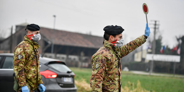 zwei Soldaten mit Mundschutz stehen auf einer Straße. einer hält eine Kelle hoch