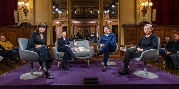 vier Menschen sitzen auf Polstermöbeln auf einer Bühne
