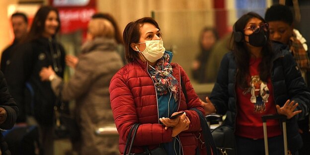 Menschen stehen mit Schutzmasken und Koffern im Mailänder Bahnhof