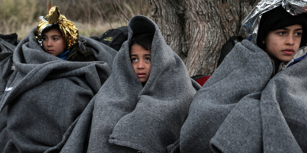 Drei Kinder sind in graue Decken gehüllt