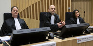 Zwei Männer und eine Frau in schwarzen Roben sitzen in einem Gerichtssaal