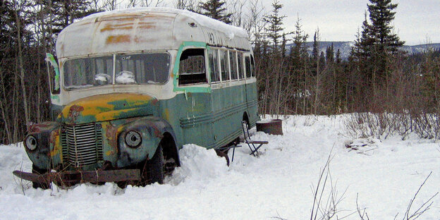 Ein alter Buss steckt mitten im Wald im Schnee fest
