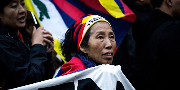 Eine Frau trägt ein Stirnband in den Fraben der tibetischen Fahne