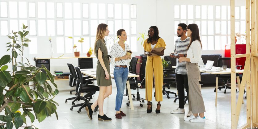 Eine Gruppe junger Menschen von unterschiedlicher Hautfarbe steht in einem Büro