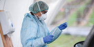 Eine Ärztin in Schutzkleidung hält einen Abstrichstäbchen in den Händen
