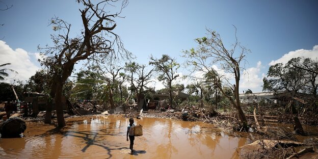 zerzauste Bäume in von braunem Wasser überfluteter LÖandschaft. in der Bildmitte ist ein Kind