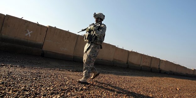Ein amerikanischer Soldat hält sein Gewehr im Anschlag und läuft an einer Mauer entlang