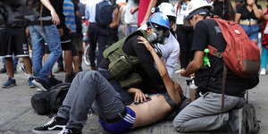 Chile: Ein Mann mit nacktem Oberkörper und blutverschmierten Armen liegt am Boden. Mehrere Männer mit Helm kümmern sich um ihn.