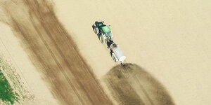Ein Traktor fährt über ein Feld und düngt. Luftaufnahme