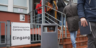 Menschen stehen auf einer Treppe vor einem Krankenhaus an