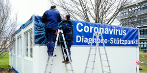 Handwerker befestigen an auf dem Gelände des Universitätsklinikums aufgestellten Containern ein Transparent mit der Aufschrift «Coronavirus Diagnose-Stützpunkt».