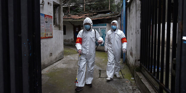 Zwei Männer in Schutzanzügen versprühen Desinfektionsmittel