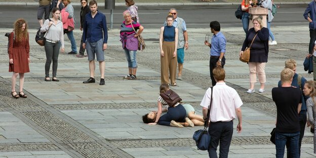 Eine Frau liegt zwischen PassantInnen leblos auf dem Boden