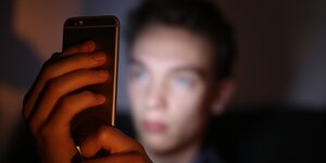 Ein Jugendlicher schaut auf sein Smartphone, das Gesicht ist unscharf und vom Display erleuchtet