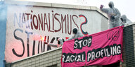 Aktivisten stehen auf einem Dach, an der Wand steht "Nationalismus stinkt", auf einem Plakat steht "Stop Racial Profiling"
