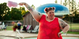 Dicke Frau an einem Pool hält eine Zuckerwatte in die Luft