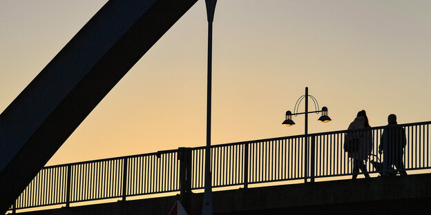 Im Abendlicht gehen zwei Menschen über eine Brücke
