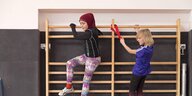 Zwei junge Mädchen beim Sportunterricht an der Sprochenwand, eins mit Kopfbedeckung, eins ohne