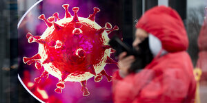 Frau vor einer Werbetafel mit der Illustration eines Coronavirus.