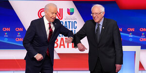 Joe Biden und Bernie Sanders berührern sich auf der Debattenbühne mit den Ellbogen