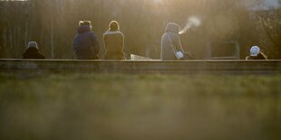 Menschen sitzen auf einer Betonmauer in einem Park