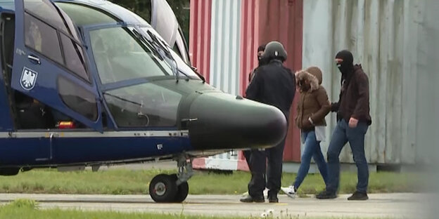Eine Frau wird von vermummten Polizisten zu einem Hubschrauber der Bundespolizei geführt.