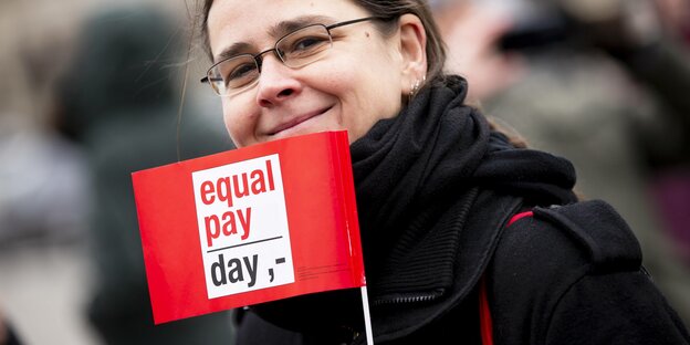 Frau mit eine Fahne, auf der "equal pay day" geschrieben steht.