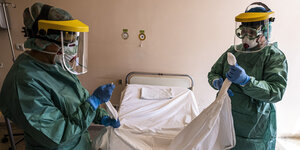 Krankenschwestern in Schutzkleidung beziehen ein Bett in einem Krankenhaus