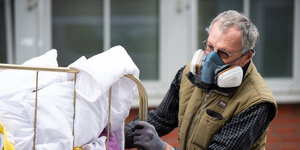 Ein Mann verlädt mit einer Atemschutzmaske Schmutzwäsche aus einer Einrichtung für Obdachlose.