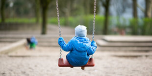 Ein Kind schaukelt auf einem leeren Spielplatz.