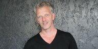 Karuna-Geschäftsführer Jörg Richert steht vor einer Wand Porträt