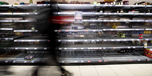 Eine Person läuft in einem Supermarkt vor einem leeren Regal.