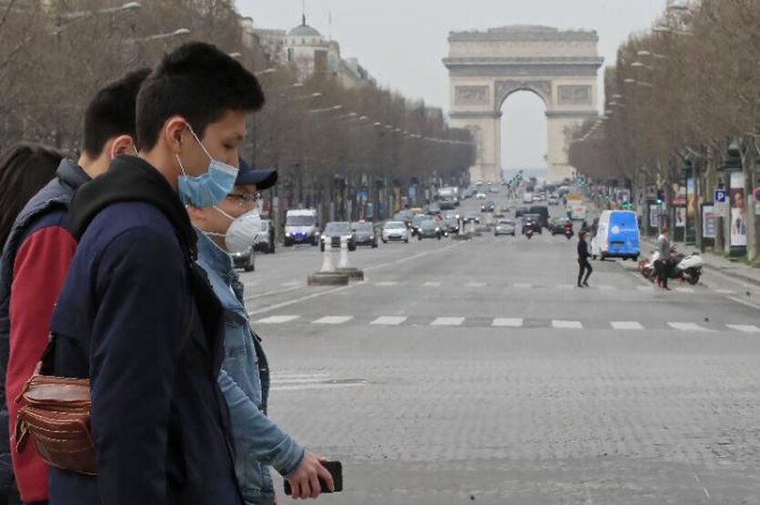 Die Einkausstraße Champs-Elysée mit dem Triumphbogen im Hintergrund. Es fahren wenige Autos und Passanten tragen Mundschutz