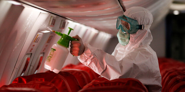Ein Mann im Schutzanzug sprüht in einem Flugzeug Desinfektionsmittel aus einer Flasche