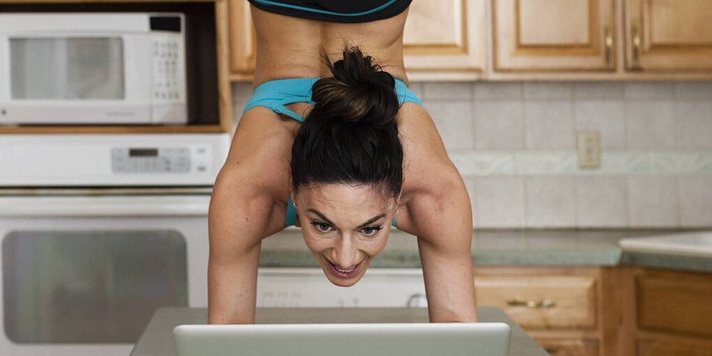 Eien Frau macht einen Handstand vor ihrem Laptop in der Küche