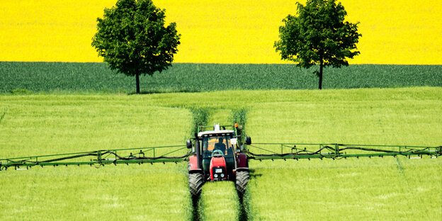 Ein Traktor fähr über ein Gerstenfeldund versprüht Pflanzenschutzmittel.