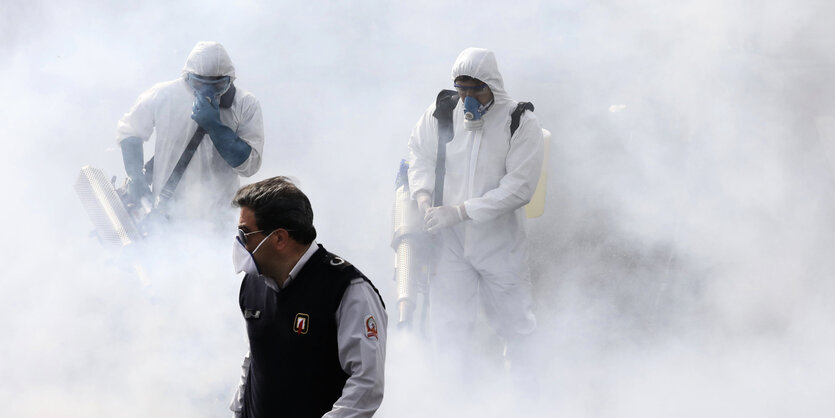 Menschen in Schutzanzügen stehen im Nebel von Desinfiktionsmittel.